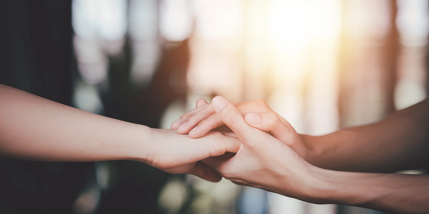 Two hands clasped together in a comforting, supportive grip against a soft, blurred background.